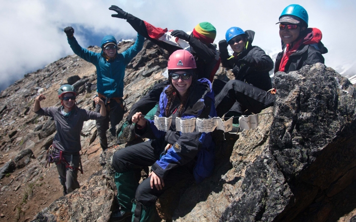a group of outward bound students wearing safety gear appear to celebrate at the top of the mountain